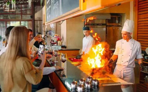 Cuisine ouverte d'un restaurant, chefs en action avec des flammes impressionnantes. Des clients prennent des photos, respectant la norme.