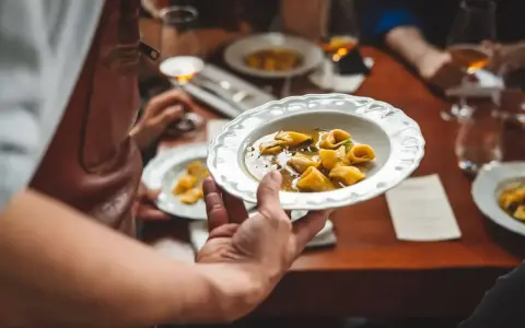 Un serveur présente une assiette de tortellinis dans un bouillon. Le service en restauration est à son apogée.