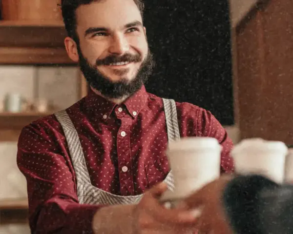 Barista souriant, chemise à motif CDD, sert un café.