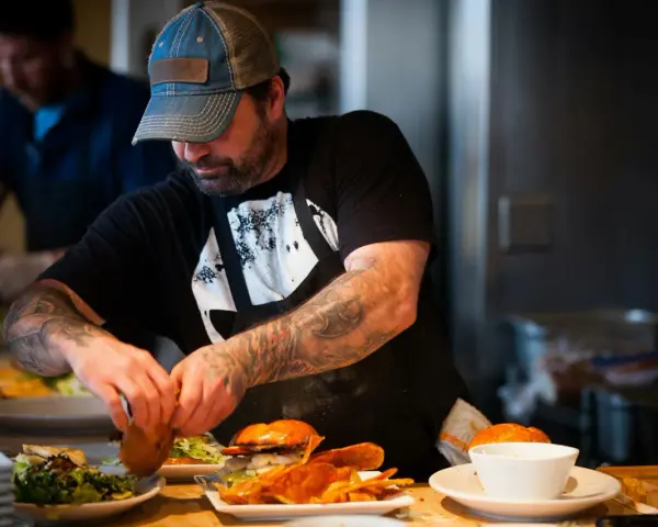 Un chef tatoué prépare des burgers et des frites, gage d'assurance restauration rapide.