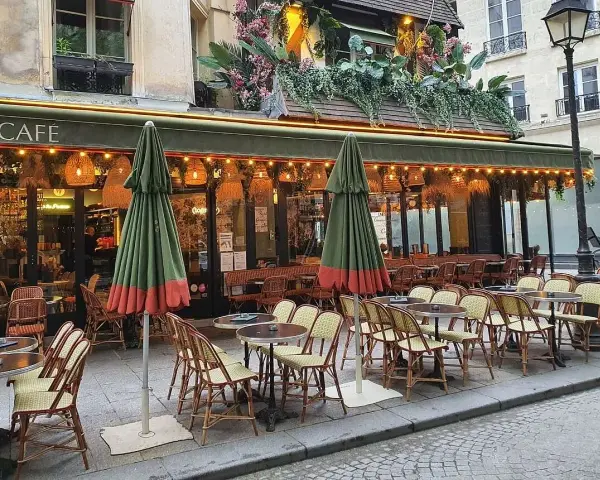 Terrasse de café parisien, tables et chaises en rotin, parasols verts. La réglementation terrasse sur trottoir est respectée.