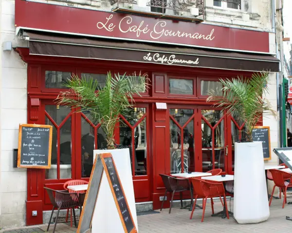 Le Café Gourmand, un restaurant aux noms originaux, invite à la dégustation avec sa façade rouge vif et ses palmiers.