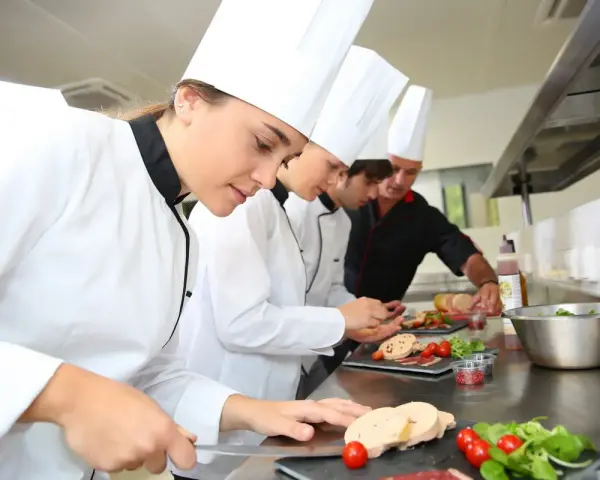 Des chefs apprennent à travailler dans un restaurant, préparant des plats avec soin.