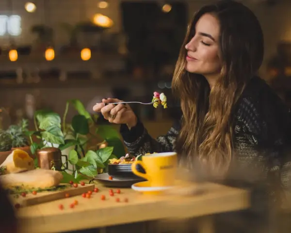 Une femme savoure un plat de pâtes dans un restaurant. Son expression suggère un avis très positif sur le repas.