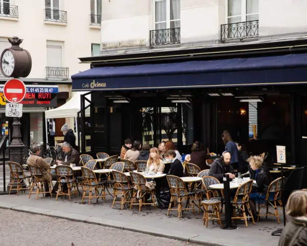Terrasse animée d'un restaurant parisien, le Café Delmas, où des clients profitent de l'extérieur. Pas de tapage nocturne ici, juste une ambiance de bistrot paisible.