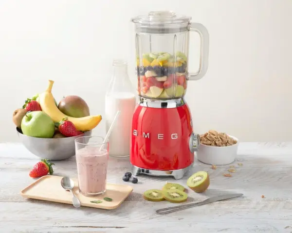 Un blender rouge SMEG, rempli de fruits, prêt à préparer un smoothie. Il montre à quoi sert un blender : mixer des ingrédients pour des boissons saines et délicieuses.