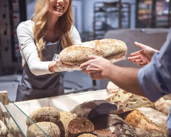 Une boulangère souriante offre une miche de pain frais, célébrant la journée mondiale de la pâtisserie.