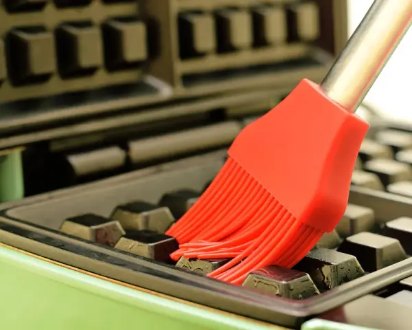 Un pinceau rouge nettoie les recoins d'un gaufrier encrassé.