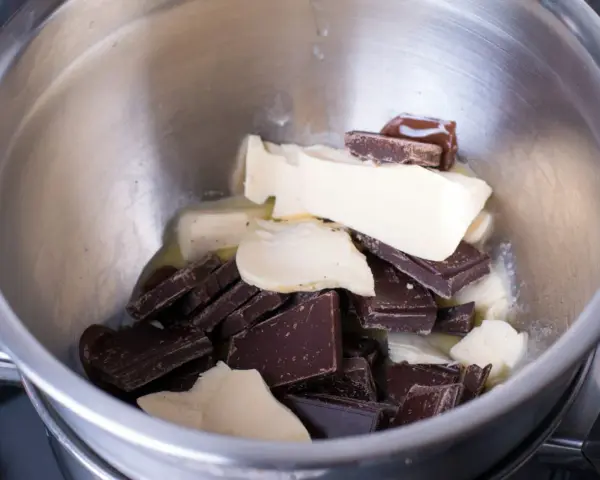 Morceaux de chocolat noir et de beurre dans un bol en métal, prêts pour une cuisson au bain-marie au four.