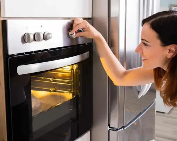 Une femme ajuste le bouton du four pour savoir à quelle température faire réchauffer un plat. Le plat est visible à travers la vitre.