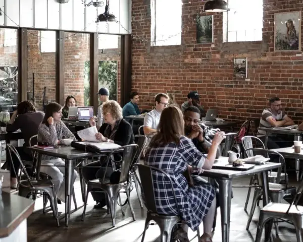 Ambiance de café animée, des gens travaillent et discutent. Un dimanche payé double pour la restauration, l'atmosphère est détendue.