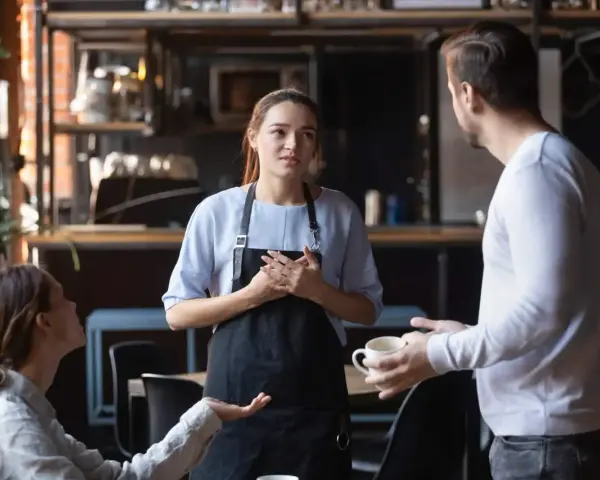 Serveuse attentive face à une cliente mécontente exprimant sa frustration. La serveuse écoute avec empathie.
