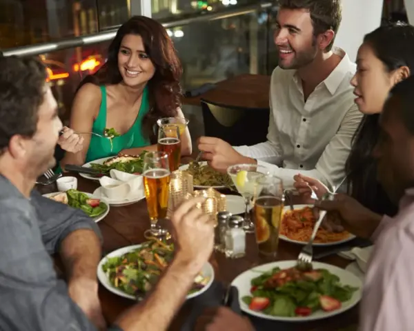 Un groupe d'amis partage un repas animé dans un restaurant, une excellente idée soirée à thème restaurant. Ils rient et discutent autour d'une table garnie de plats et de boissons.