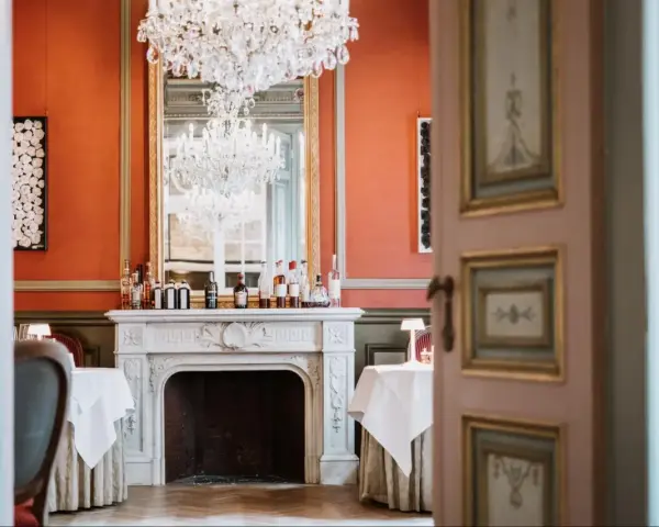 Salle à manger élégante avec cheminée, lustres et tables dressées. Un décor parfait pour savoir comment être référencé dans le Petit Futé.