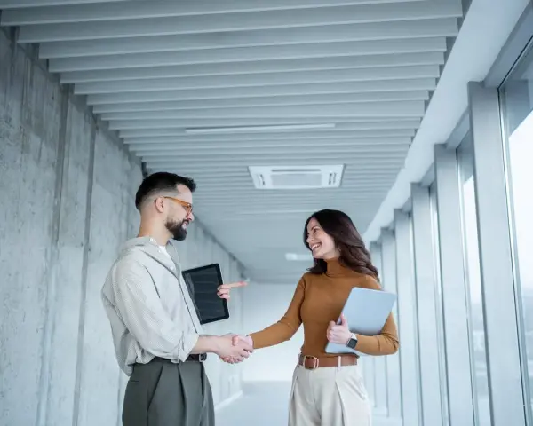 Un homme et une femme se serrent la main dans un couloir moderne, signe d'une prime cooptation réussie.
