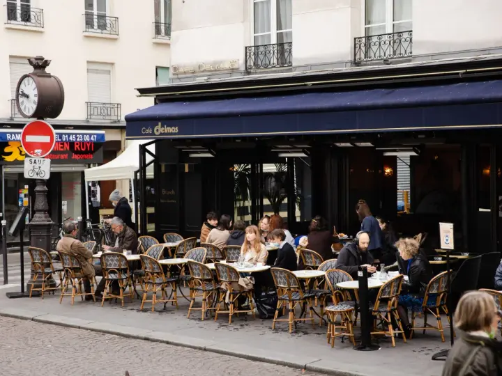 Terrasse animée d'un restaurant parisien, le Café Delmas, où des clients profitent de l'extérieur. Pas de tapage nocturne ici, juste une ambiance de bistrot paisible.