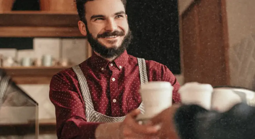 Barista souriant, chemise à motif CDD, sert un café.