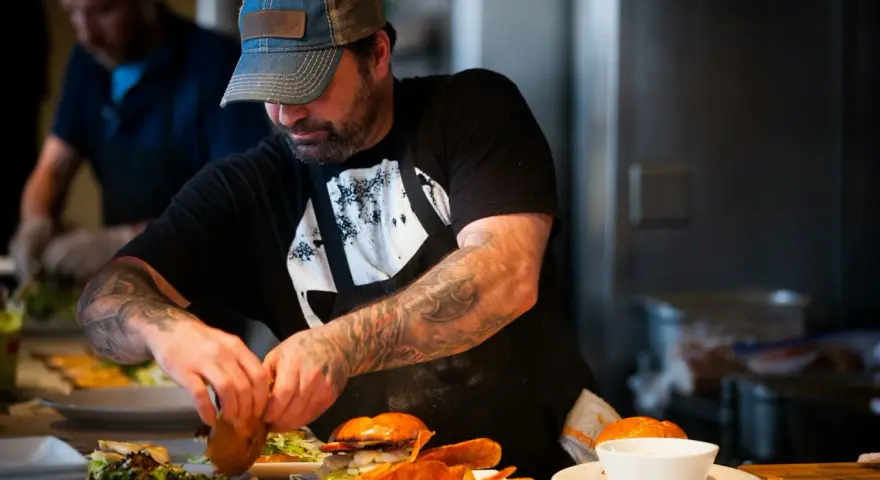 Un chef tatoué prépare des burgers et des frites, gage d'assurance restauration rapide.