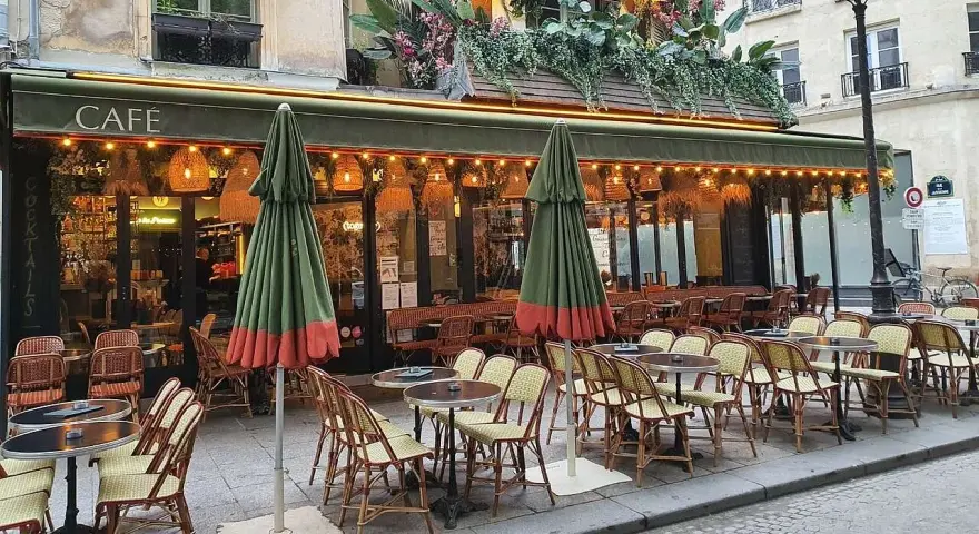 Terrasse de café parisien, tables et chaises en rotin, parasols verts. La réglementation terrasse sur trottoir est respectée.