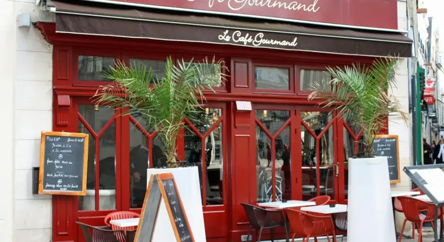 Le Café Gourmand, un restaurant aux noms originaux, invite à la dégustation avec sa façade rouge vif et ses palmiers.