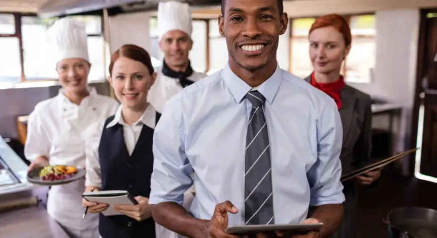 Une équipe souriante en cuisine, le responsable vérifie l'horaire collectif de travail sur sa tablette.