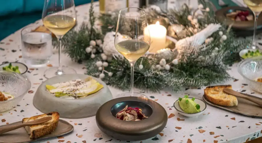 Une table dressée pour une fete gastronomique, avec des verres de vin, des amuse-bouches et une décoration hivernale.