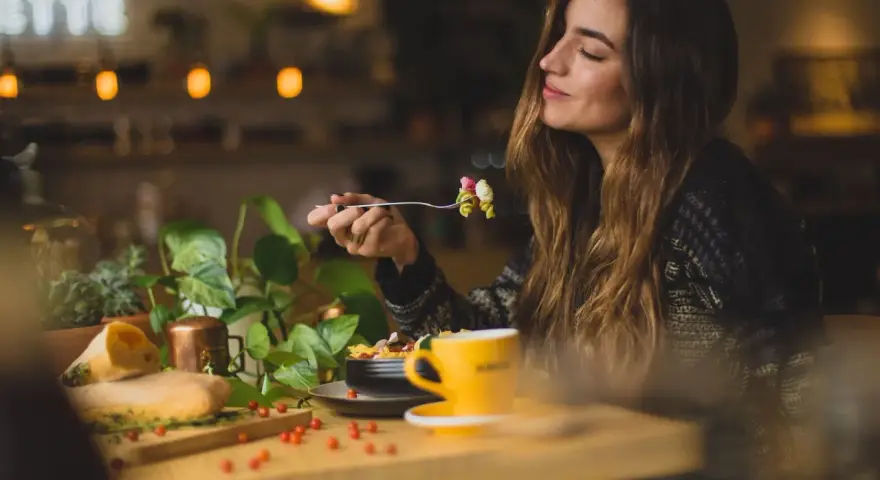 Une femme savoure un plat de pâtes dans un restaurant. Son expression suggère un avis très positif sur le repas.
