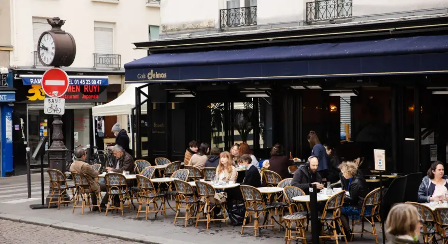 Terrasse animée d'un restaurant parisien, le Café Delmas, où des clients profitent de l'extérieur. Pas de tapage nocturne ici, juste une ambiance de bistrot paisible.