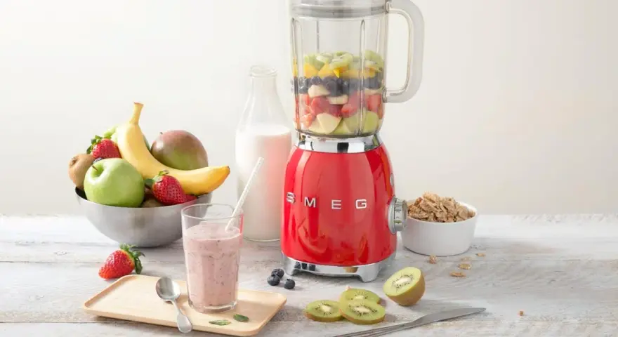 Un blender rouge SMEG, rempli de fruits, prêt à préparer un smoothie. Il montre à quoi sert un blender : mixer des ingrédients pour des boissons saines et délicieuses.