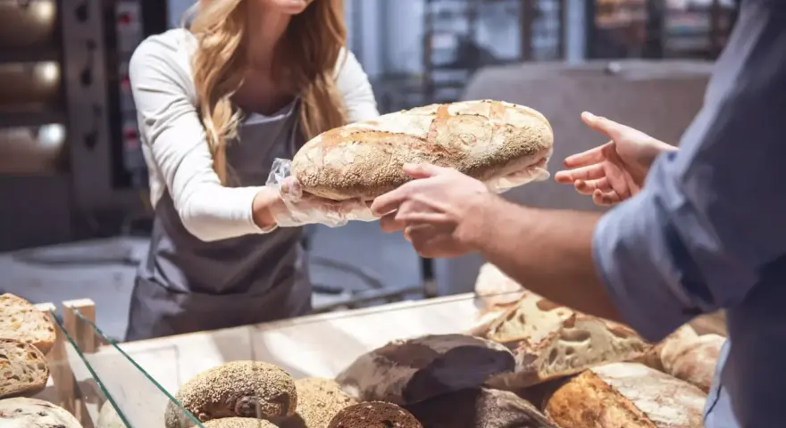 Une boulangère souriante offre une miche de pain frais, célébrant la journée mondiale de la pâtisserie.