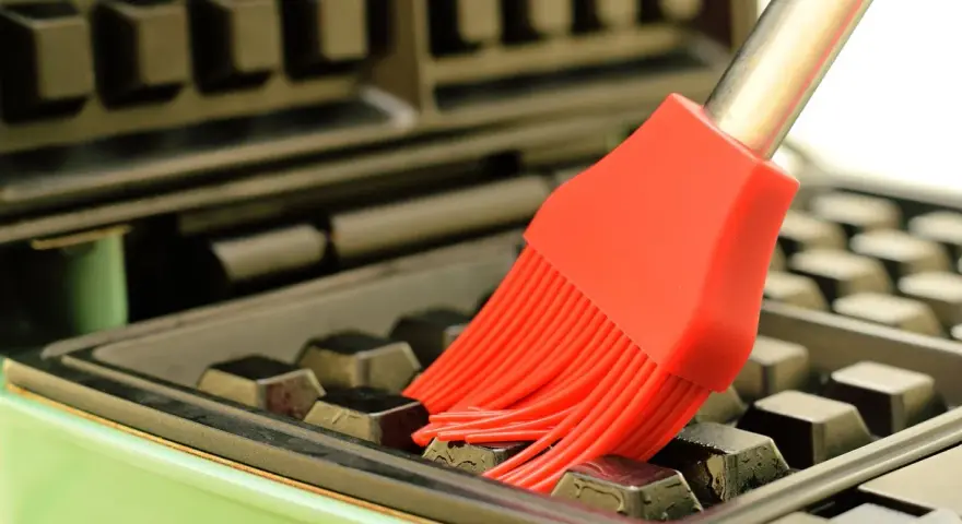 Un pinceau rouge nettoie les recoins d'un gaufrier encrassé.