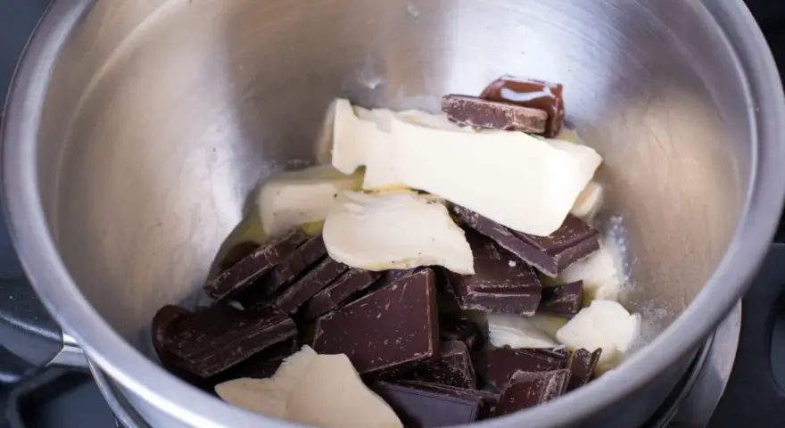 Morceaux de chocolat noir et de beurre dans un bol en métal, prêts pour une cuisson au bain-marie au four.