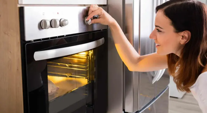 Une femme ajuste le bouton du four pour savoir à quelle température faire réchauffer un plat. Le plat est visible à travers la vitre.