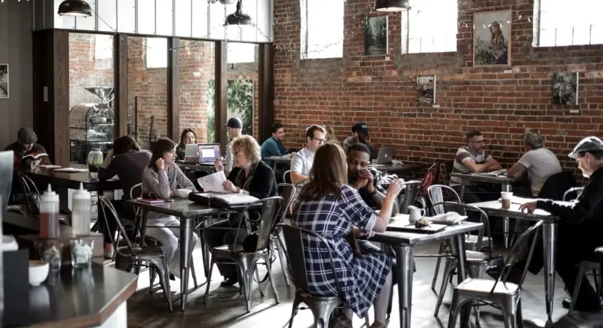 Ambiance de café animée, des gens travaillent et discutent. Un dimanche payé double pour la restauration, l'atmosphère est détendue.