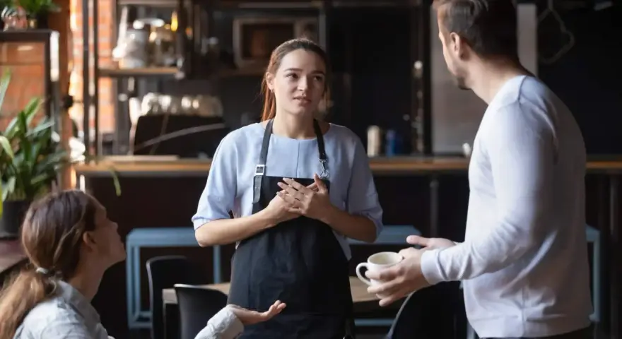Serveuse attentive face à une cliente mécontente exprimant sa frustration. La serveuse écoute avec empathie.