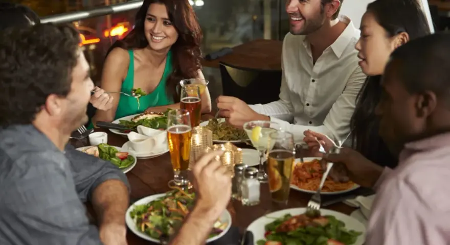 Un groupe d'amis partage un repas animé dans un restaurant, une excellente idée soirée à thème restaurant. Ils rient et discutent autour d'une table garnie de plats et de boissons.