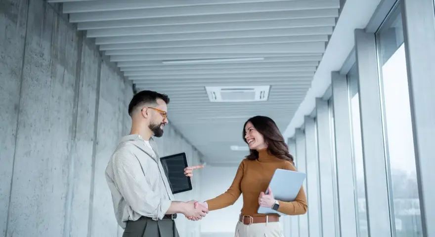 Un homme et une femme se serrent la main dans un couloir moderne, signe d'une prime cooptation réussie.
