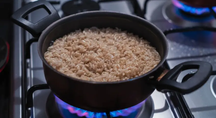 Un pot de riz brun est chauffé doucement sur une cuisinière à gaz, les flammes bleues dansant sous le récipient, pour réchauffer du riz au bain-marie.