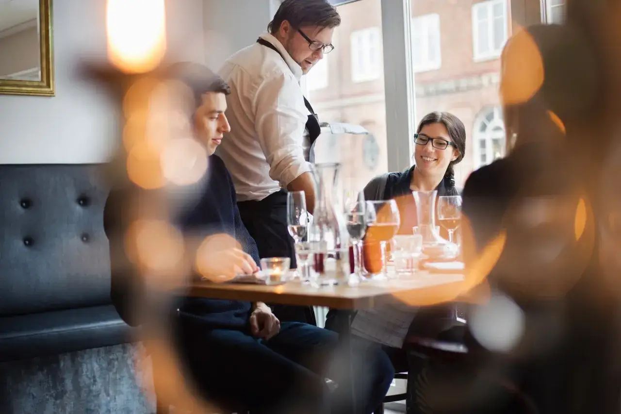 Un serveur attentif, des clients souriants. Une scène de restaurant qui illustre parfaitement les outils de fidélisation client.
