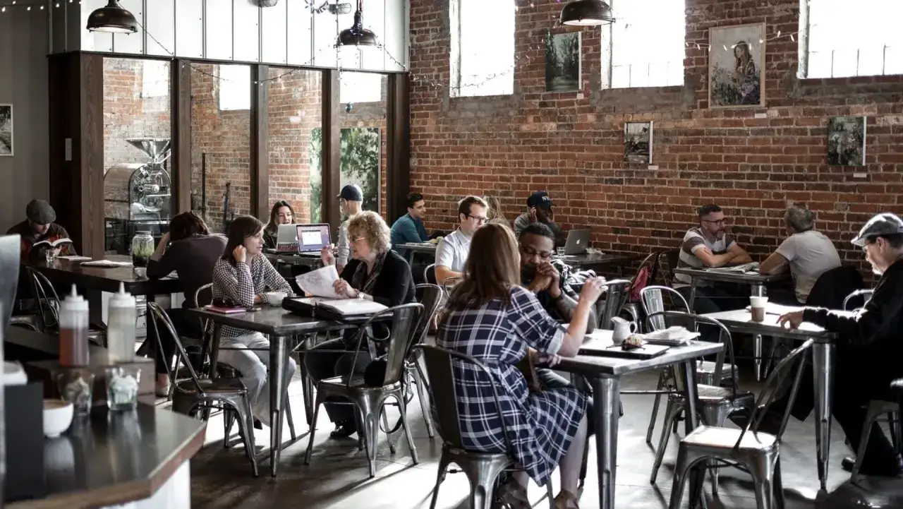 Ambiance de café animée, des gens travaillent et discutent. Un dimanche payé double restauration, parfait pour se détendre.