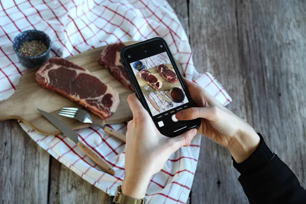 Un food influencer capture des steaks persillés sur une planche en bois, prêt à être assaisonnés.
