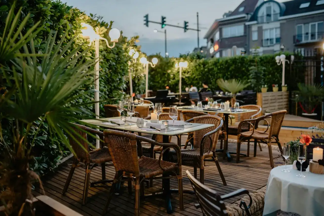 Terrasse de restaurant avec tables dressées, éclairage doux et verdure. Un cadre idéal pour optimiser le ratio de productivité des dîners en terrasse.