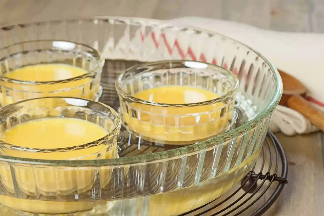 Trois ramequins remplis d'une pr&eacute;paration jaune sont plac&eacute;s dans un grand plat en verre, pr&ecirc;ts pour comment faire cuire au bain-marie.
