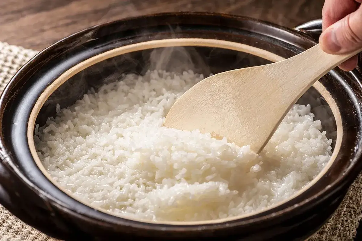 Cuillère en bois remuant du riz blanc fumant dans un pot en terre cuite, méthode pour réchauffer du riz au bain marie.