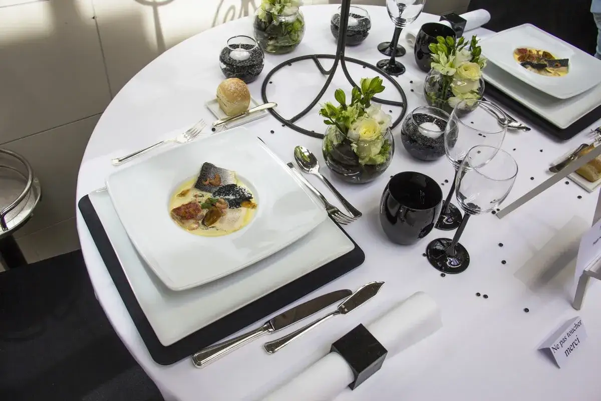 Un plat de poisson élégant, des verres à vin noirs et des fleurs ornent une table dressée pour un service en restauration.