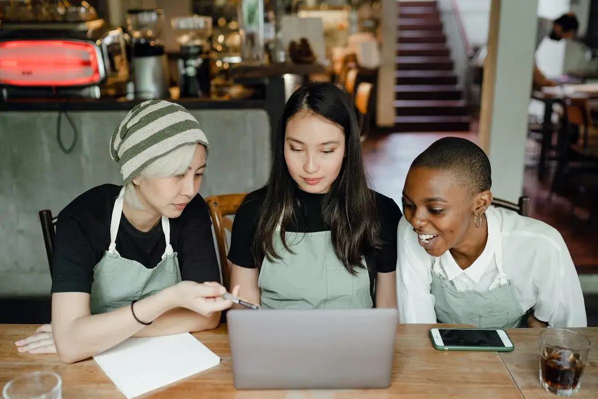 Trois jeunes femmes discutent devant un ordinateur portable, un signe de motivation au travail dans un caf&eacute;.