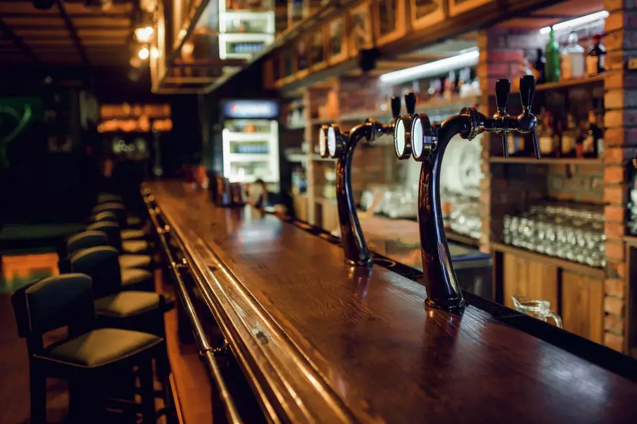 Bar en bois sombre avec tabourets, tireuses &agrave; bi&egrave;re et &eacute;tag&egrave;res remplies de bouteilles. Un lieu id&eacute;al pour servir une licence 4 alcool.