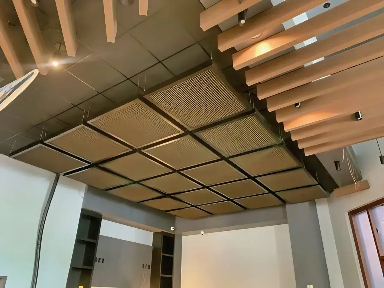 Plafond acoustique moderne avec panneaux carrés texturés et lamelles de bois. Idéal pour réduire le bruit de restaurant.