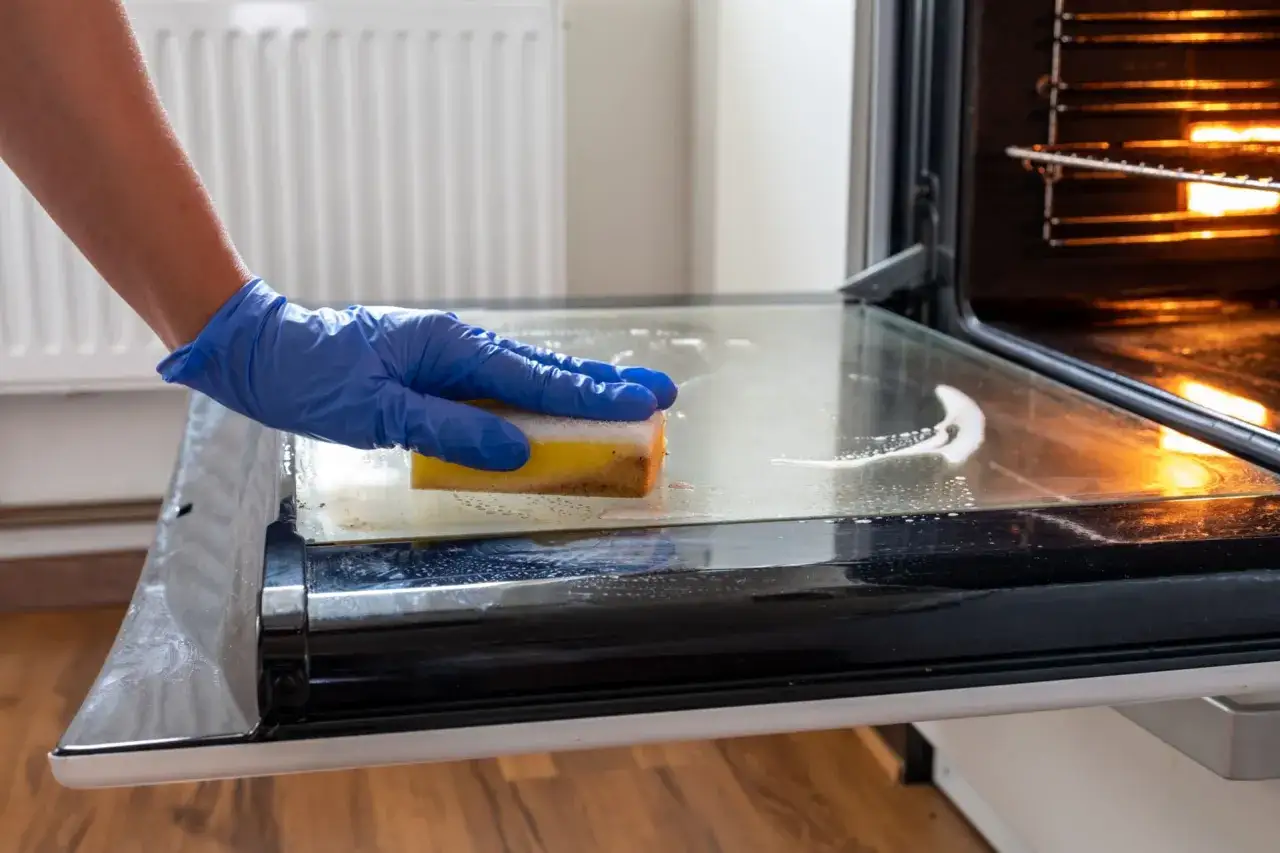 Main tenant utilise du vinaigre blanc pour nettoyer la vitre du four.