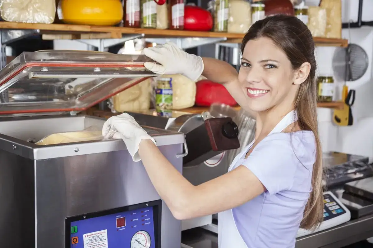 Une souriante employ&eacute;e utilise une machine sous vide pour emballer des aliments.